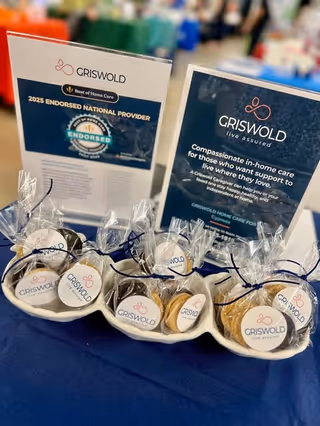 Promotional materials for Griswold Home Care, including brochures and wrapped cookies, on a blue table.