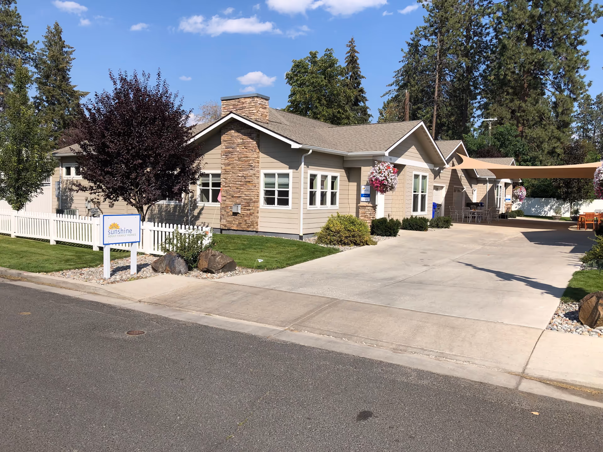 Sunshine Adult Family Home I exterior building with driveway, sign, and hanging flower baskets.
