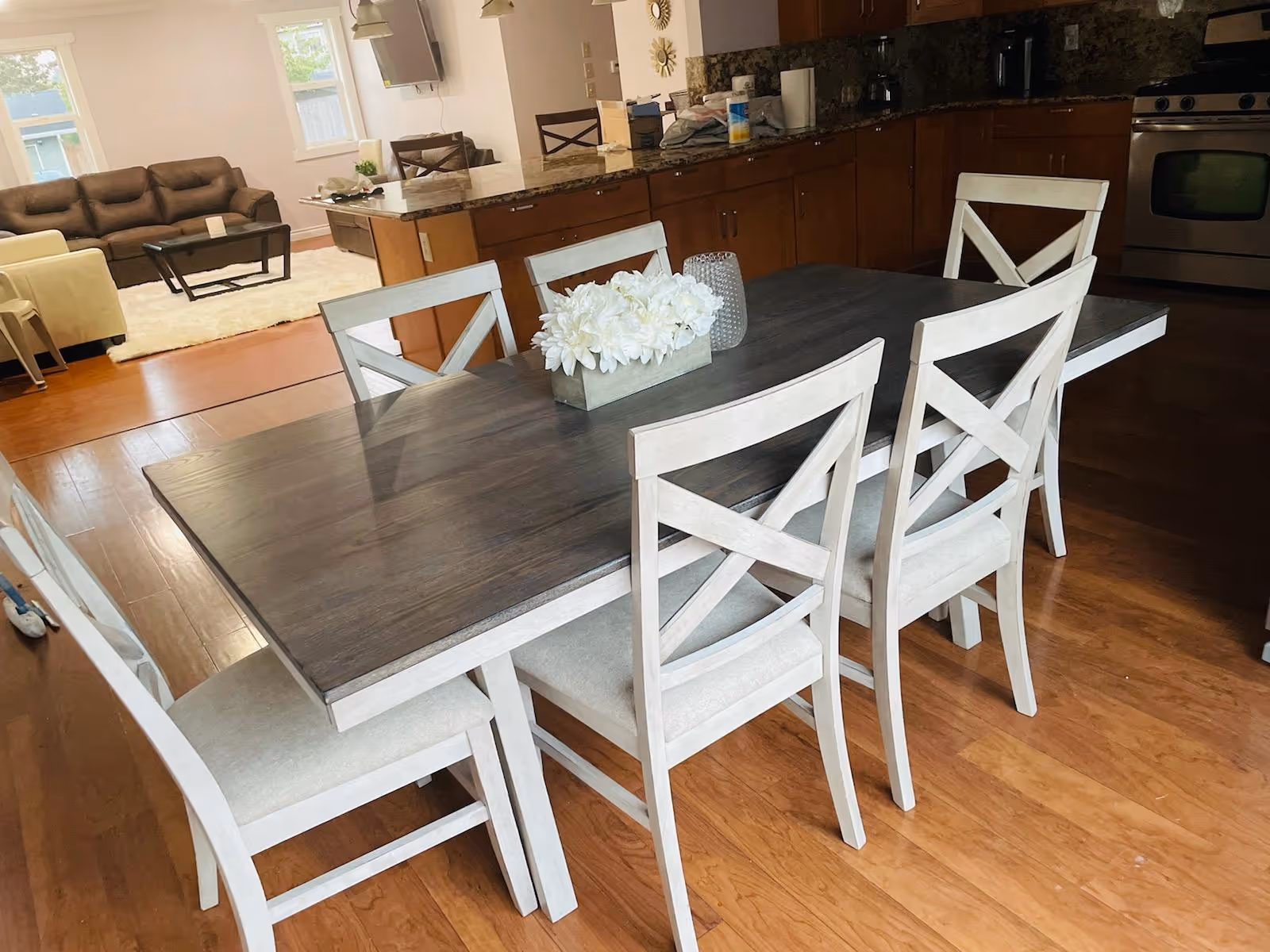 Dining room with a dark wood table and white chairs in an open kitchen area.