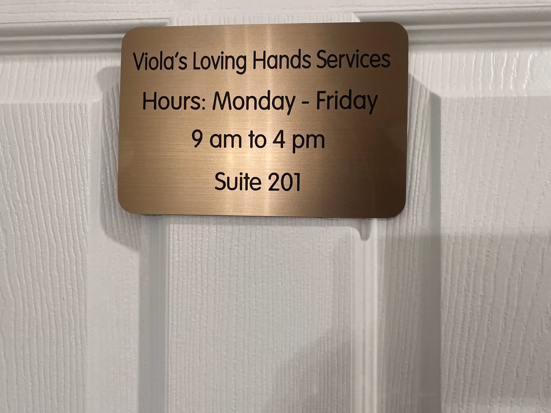 Bronze plaque on white wall displays Viola's Loving Hands Services hours and suite 201.
