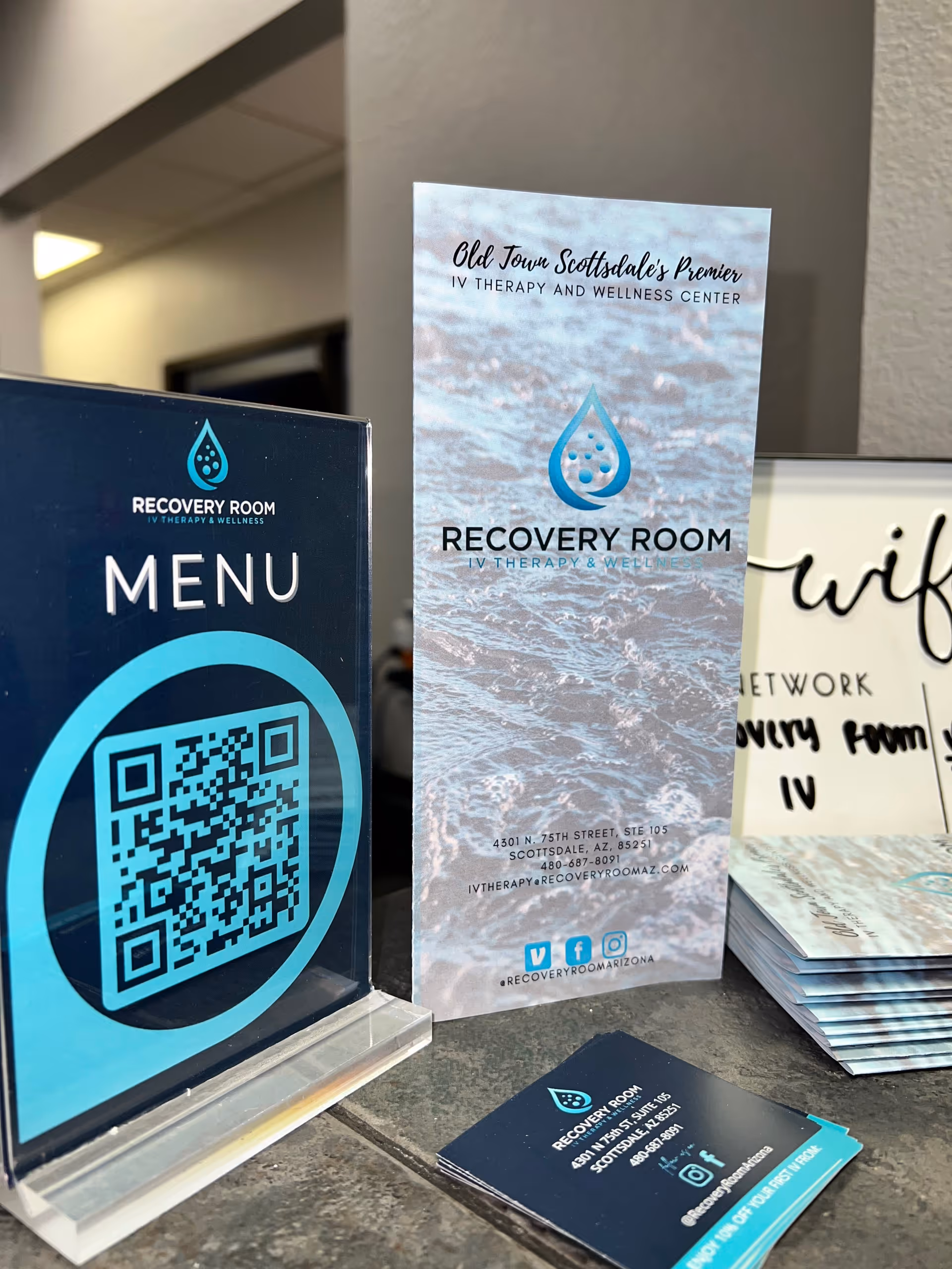 Blue and teal Recovery Room IV Therapy brochures with a QR code menu on a counter.