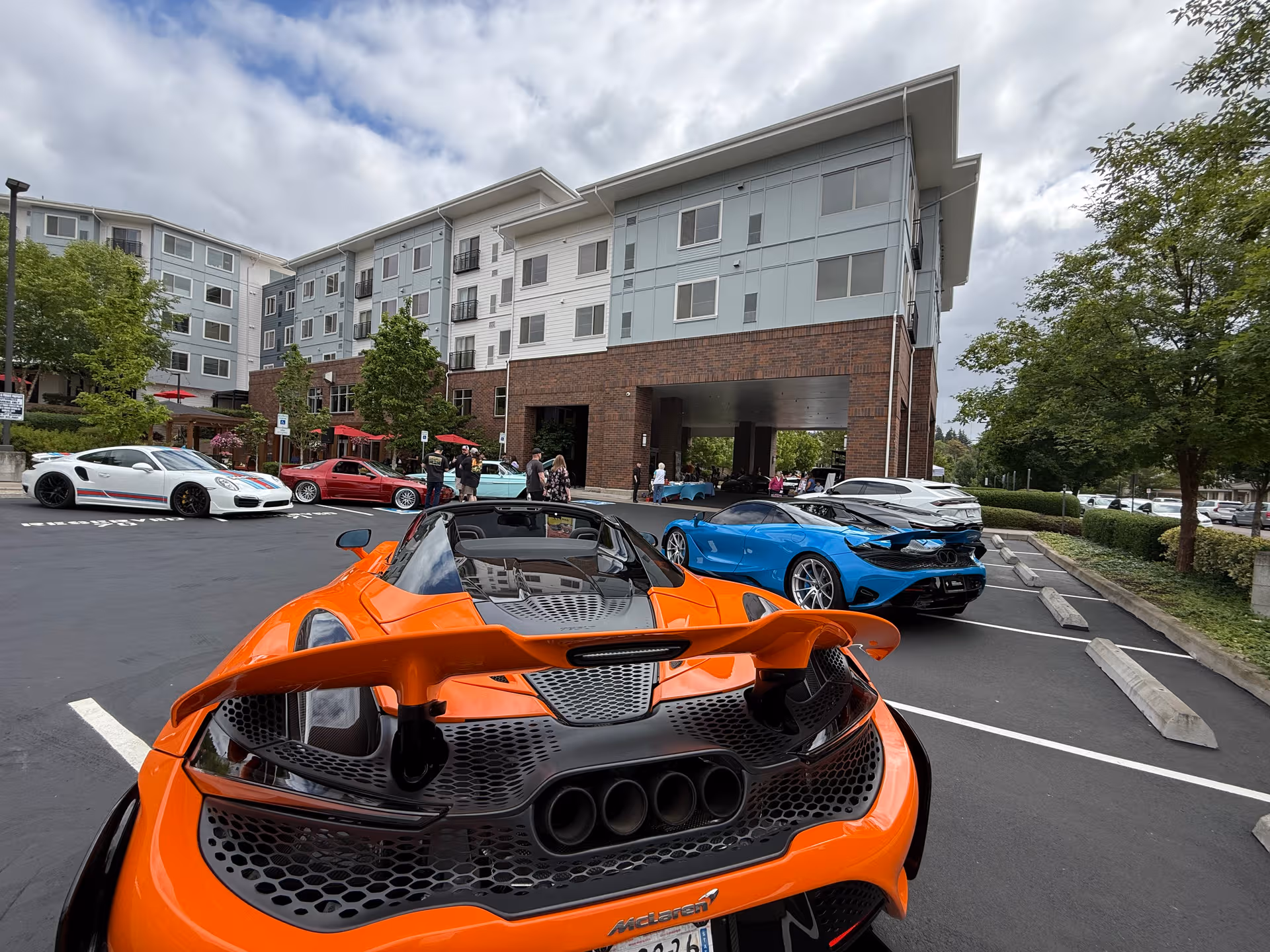 Multi-story Merrill Gardens building with a parking lot and colorful sports cars in front.