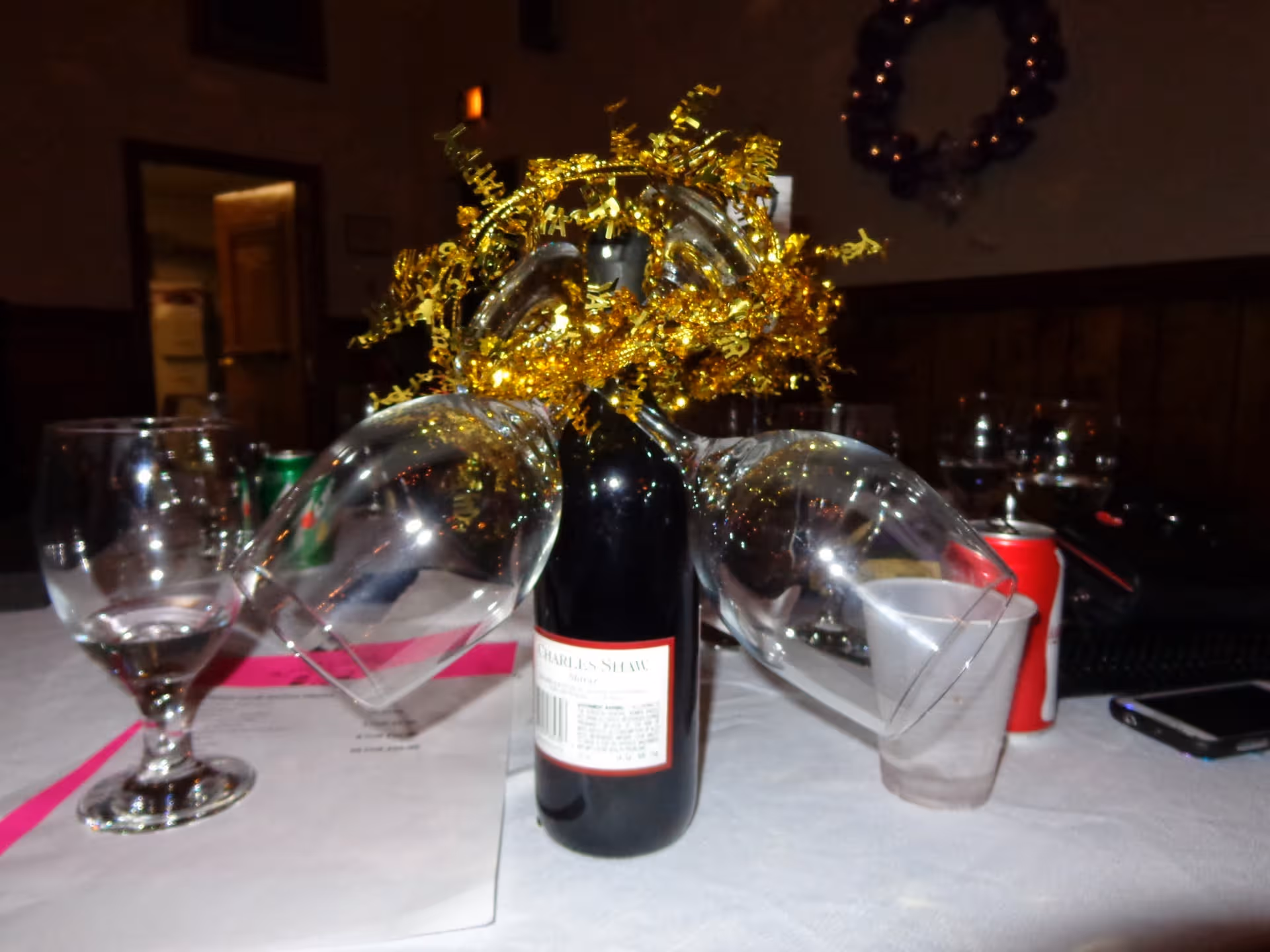 Wine bottle with gold decorative centerpiece on a table, surrounded by glasses in a dining room.