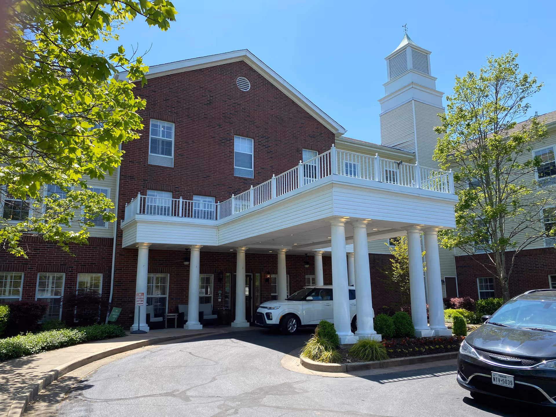 Brick senior living facility with white portico and parked cars at entrance.