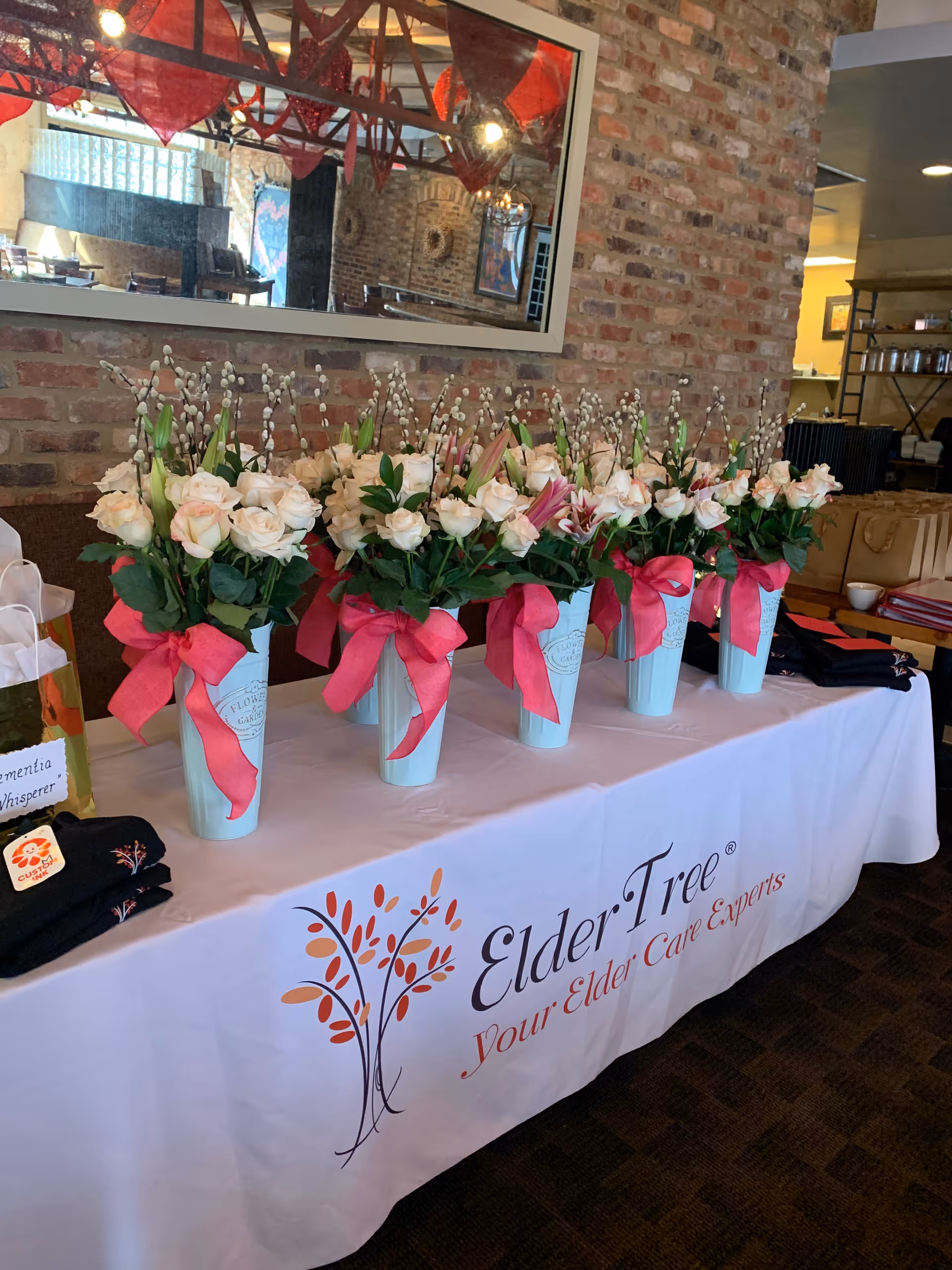 Row of pastel flowers in light blue vases with pink ribbons on a branded ElderTree table.