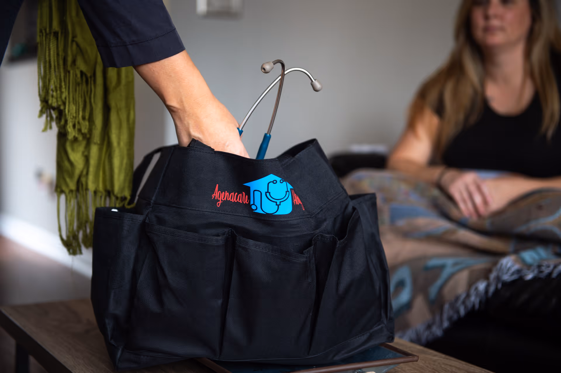 Agenacare Housecalls medical bag with stethoscope on a table beside a seated resident.
