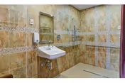 Bathroom with beige tile walls, wall-mounted sink, mirror, towel, and safety grab bars.