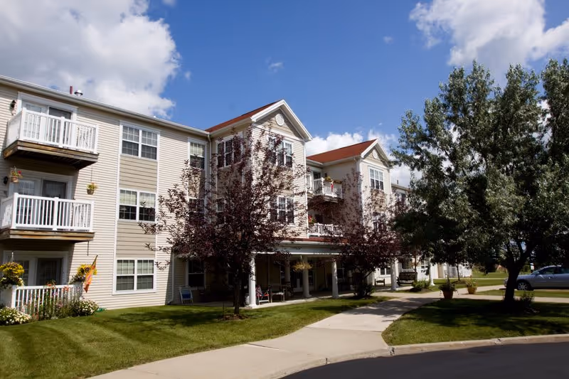 Exterior view of a multi-story senior living building with balconies and landscaped entry.