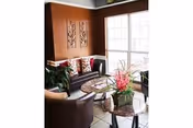 A cozy senior living lounge with couches, round tables, plants, and a large sunlit window.