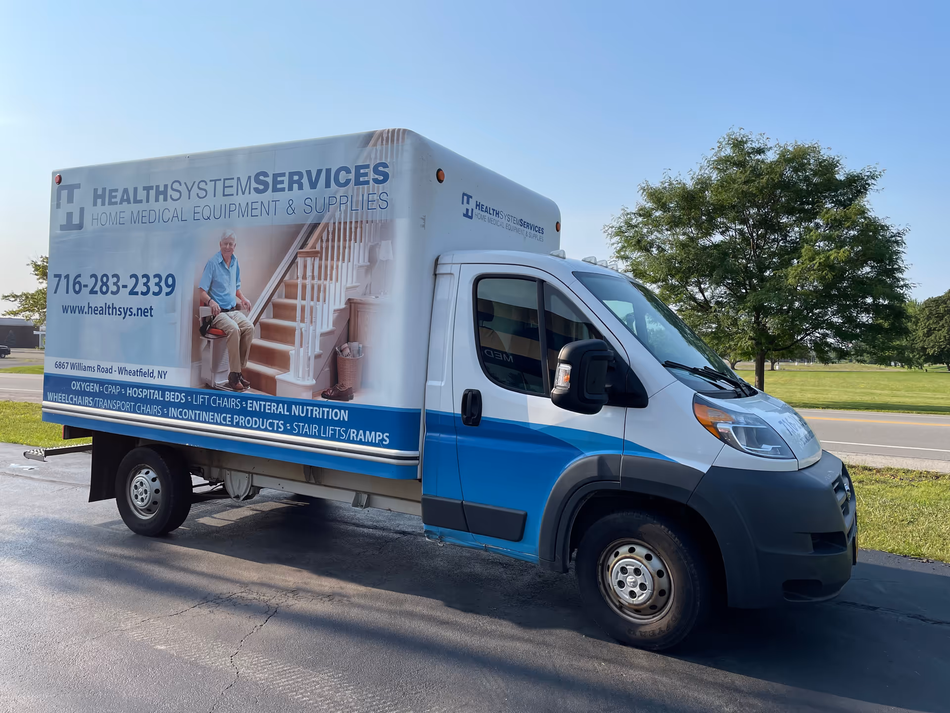 A white and blue Health System Services delivery van parked beside a road.