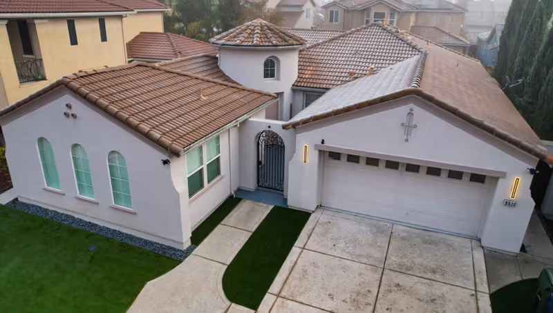 Aerial view of a tan stucco house with red tile roofs and a two-car garage.