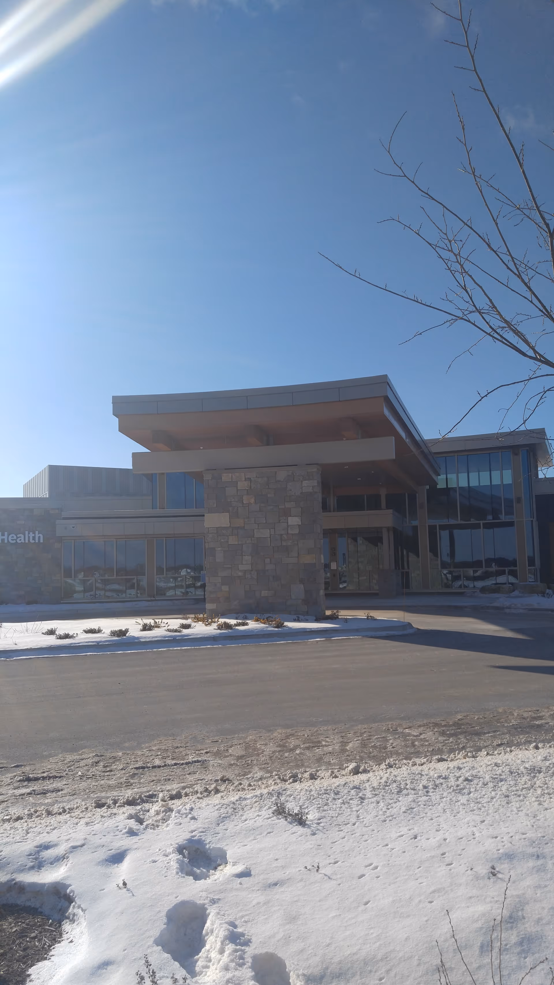 Spooner Health exterior entrance with stone pillar and glass facade on a snowy day