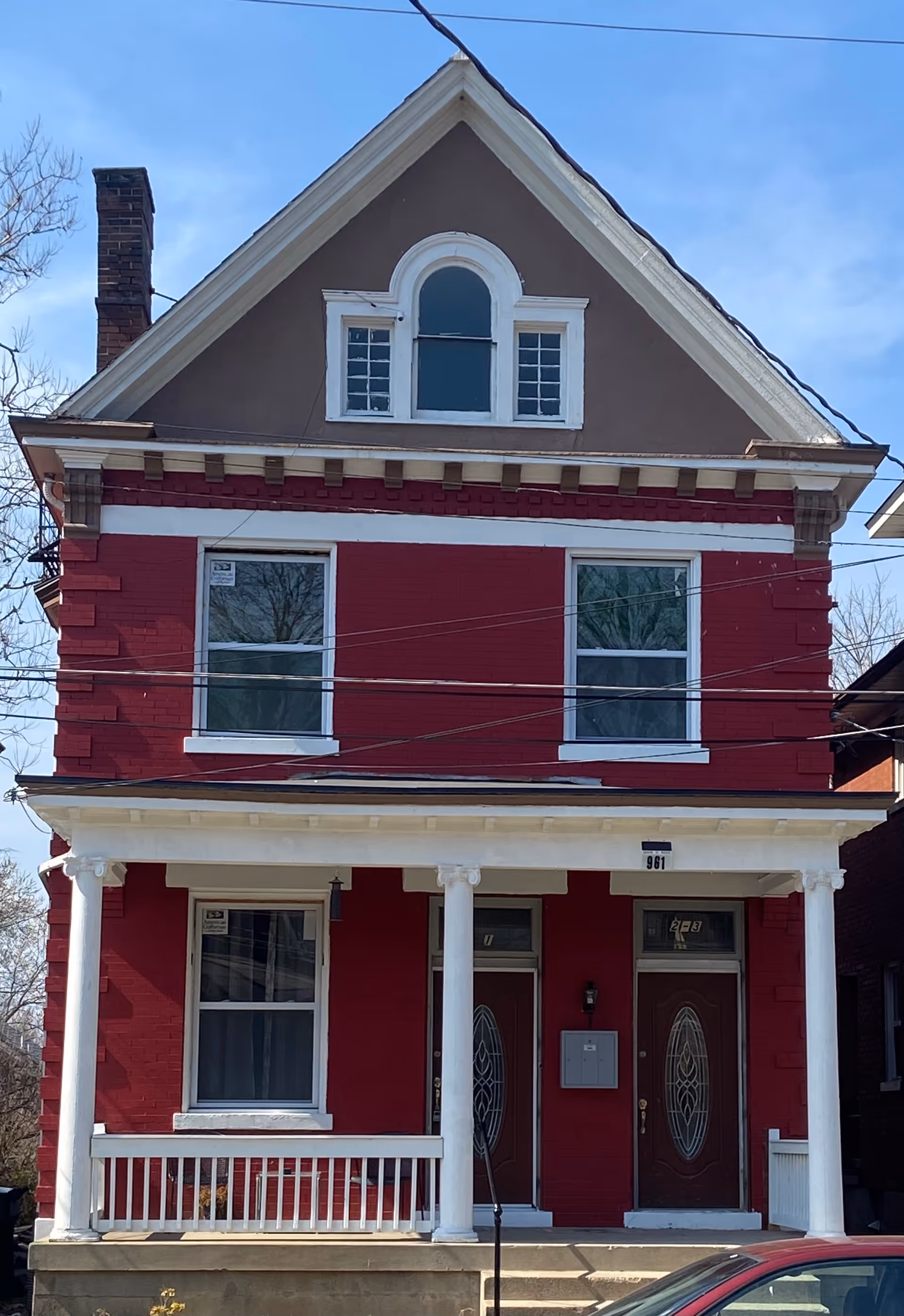 Two-story red building with white porch columns and two front doors.