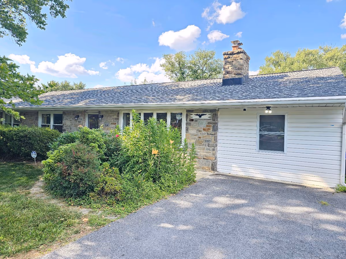 Single-story stone-and-siding senior living facility exterior with a driveway and shrubs.