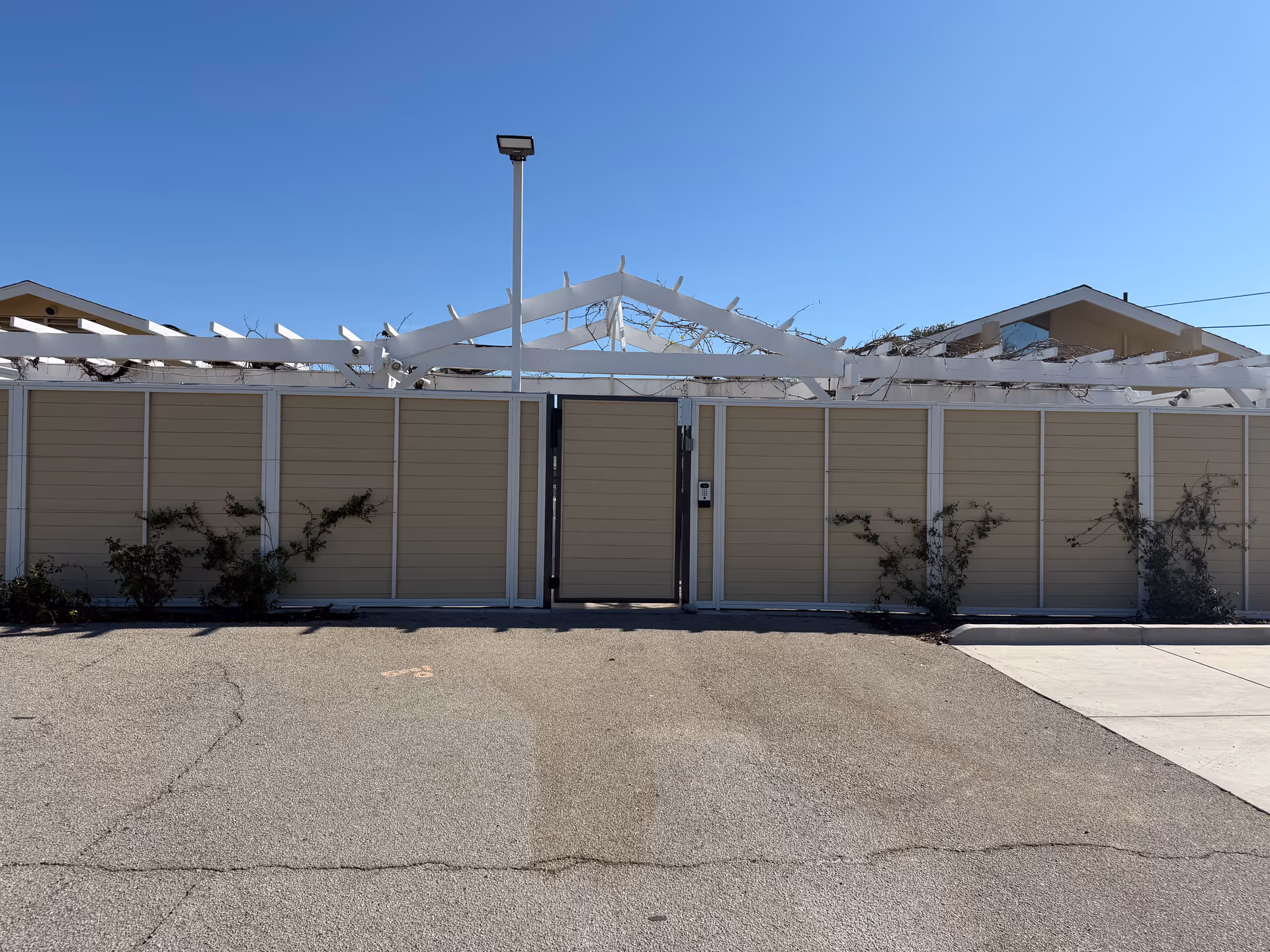 Beige exterior fence with a central gate and white framework under a clear blue sky
