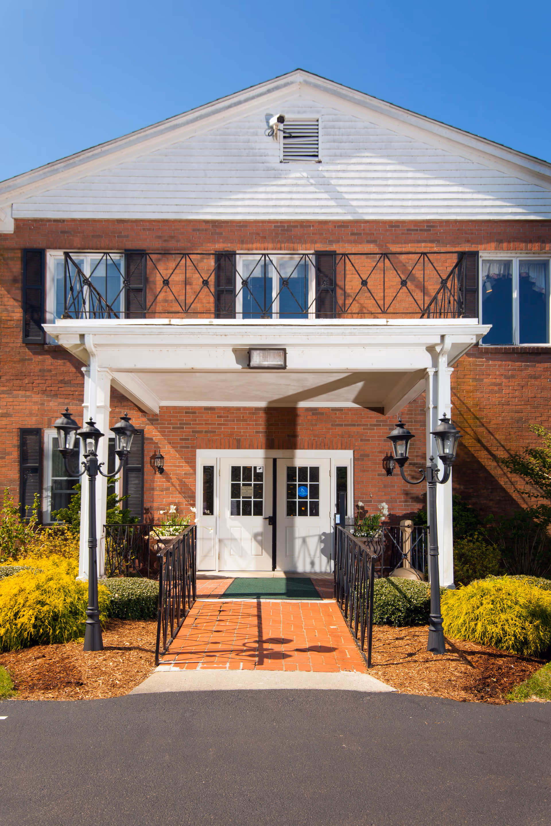 Brick nursing home entrance with white portico, double doors, and decorative lanterns.