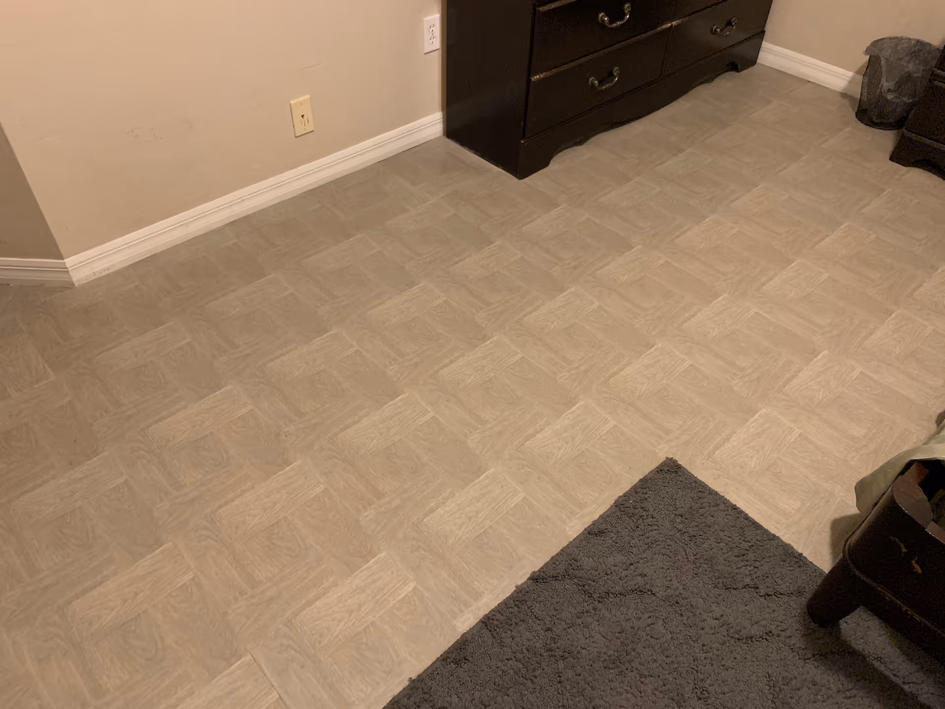 Corner of a beige interior room with dresser and patterned vinyl flooring.