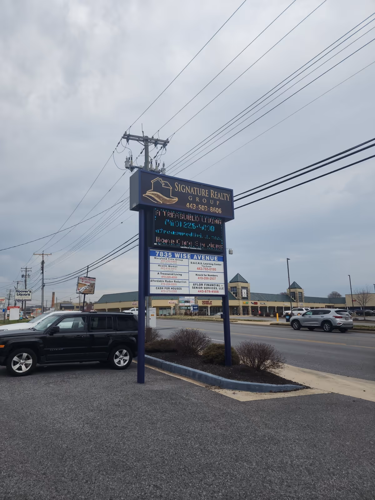 Tall blue Signature Realty Group sign in a parking lot with power lines overhead.