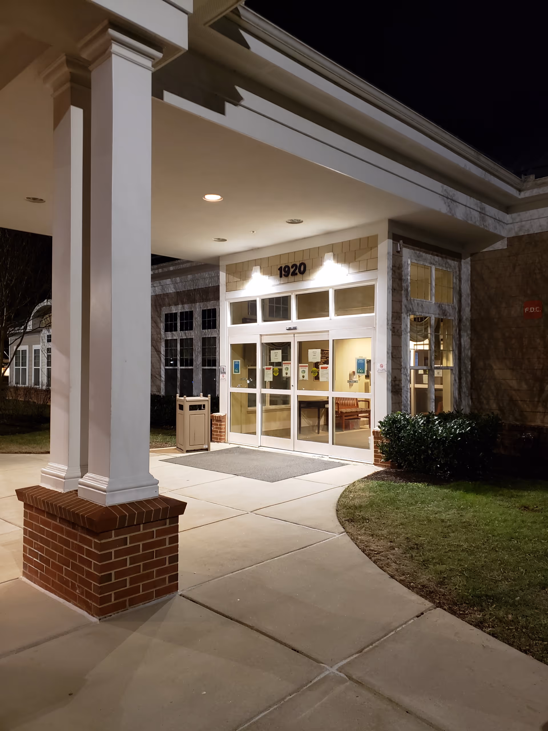 Night exterior of a senior care facility entrance with glass doors under a covered portico.