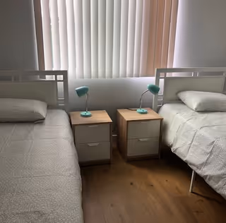Two twin beds with matching nightstands and teal lamps in a bright bedroom.