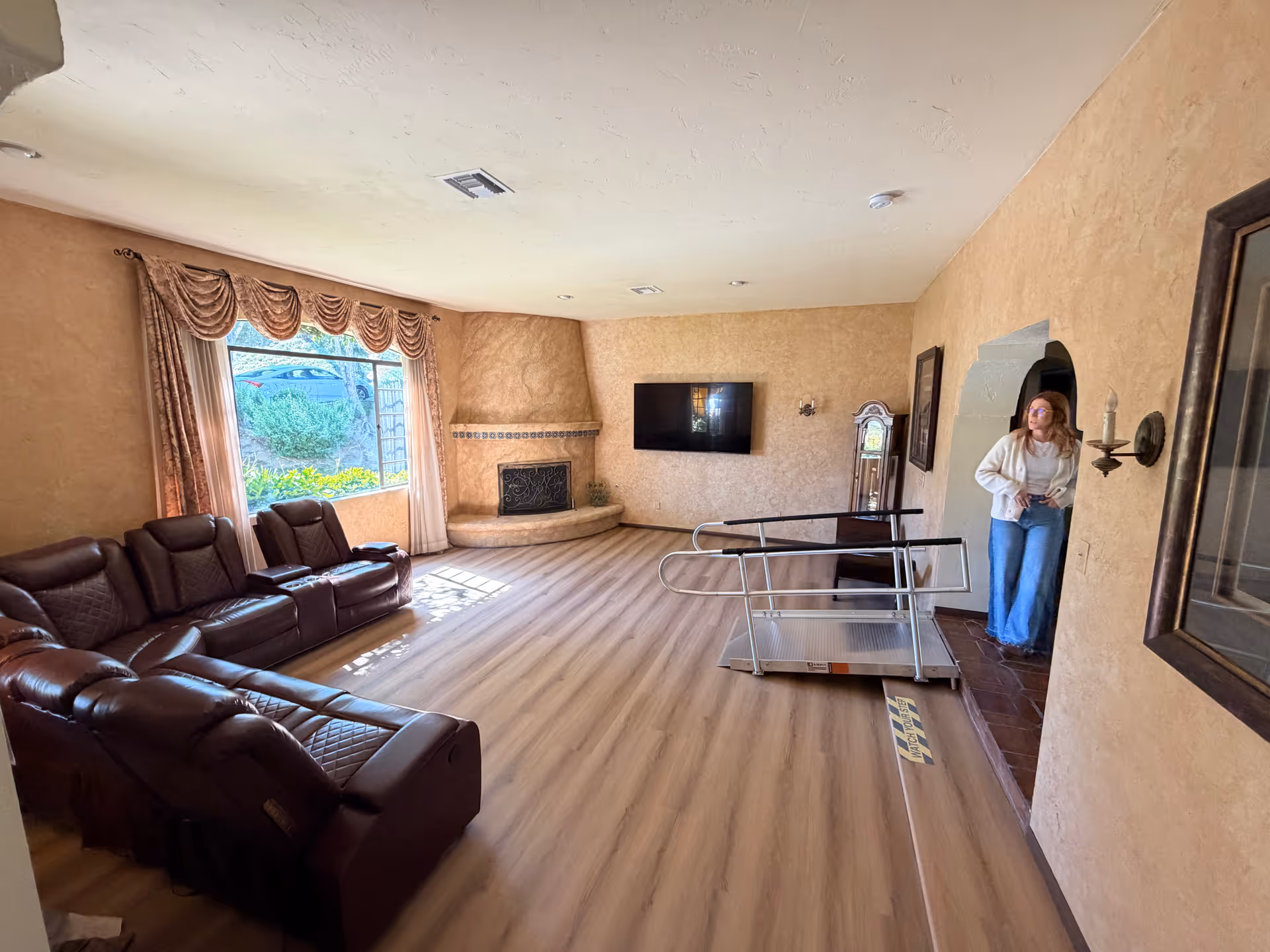 Spacious living room with leather seating, fireplace, wall-mounted TV, and a person near an archway.