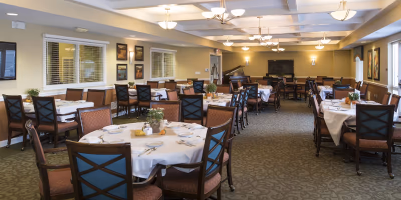 Large dining room with round tables covered in white tablecloths, set with plates and chairs.