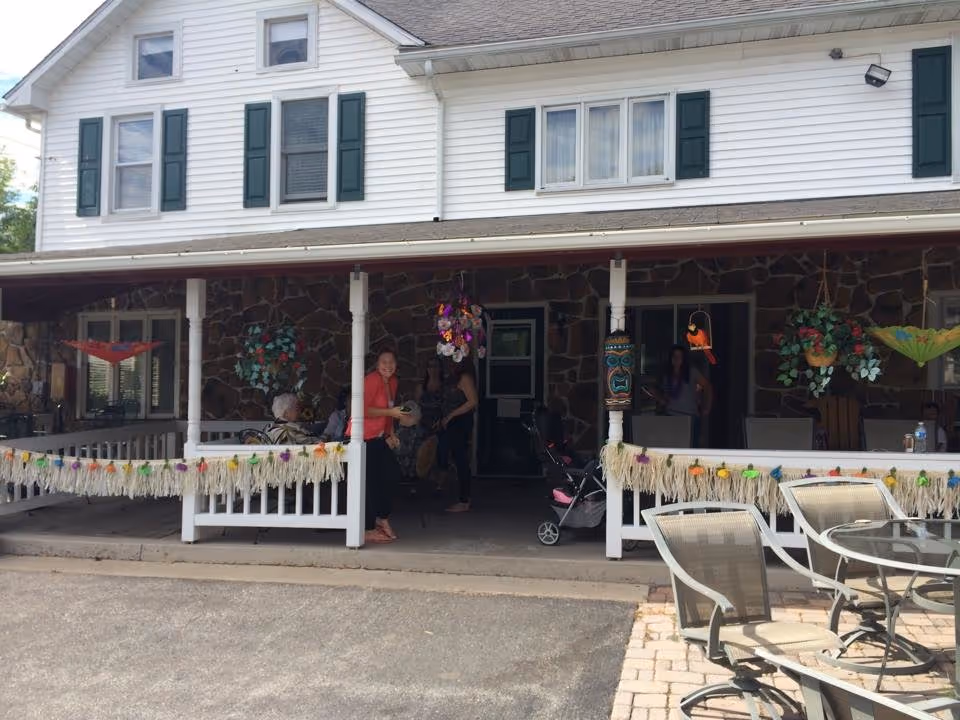 Two-story Getz Personal Care Home exterior with stone porch and people gathered on the front deck.