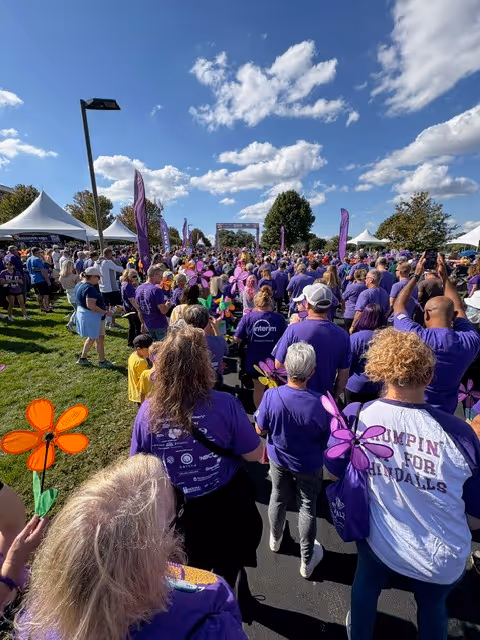 Large crowd wearing purple at an outdoor event with tents and windmill props.