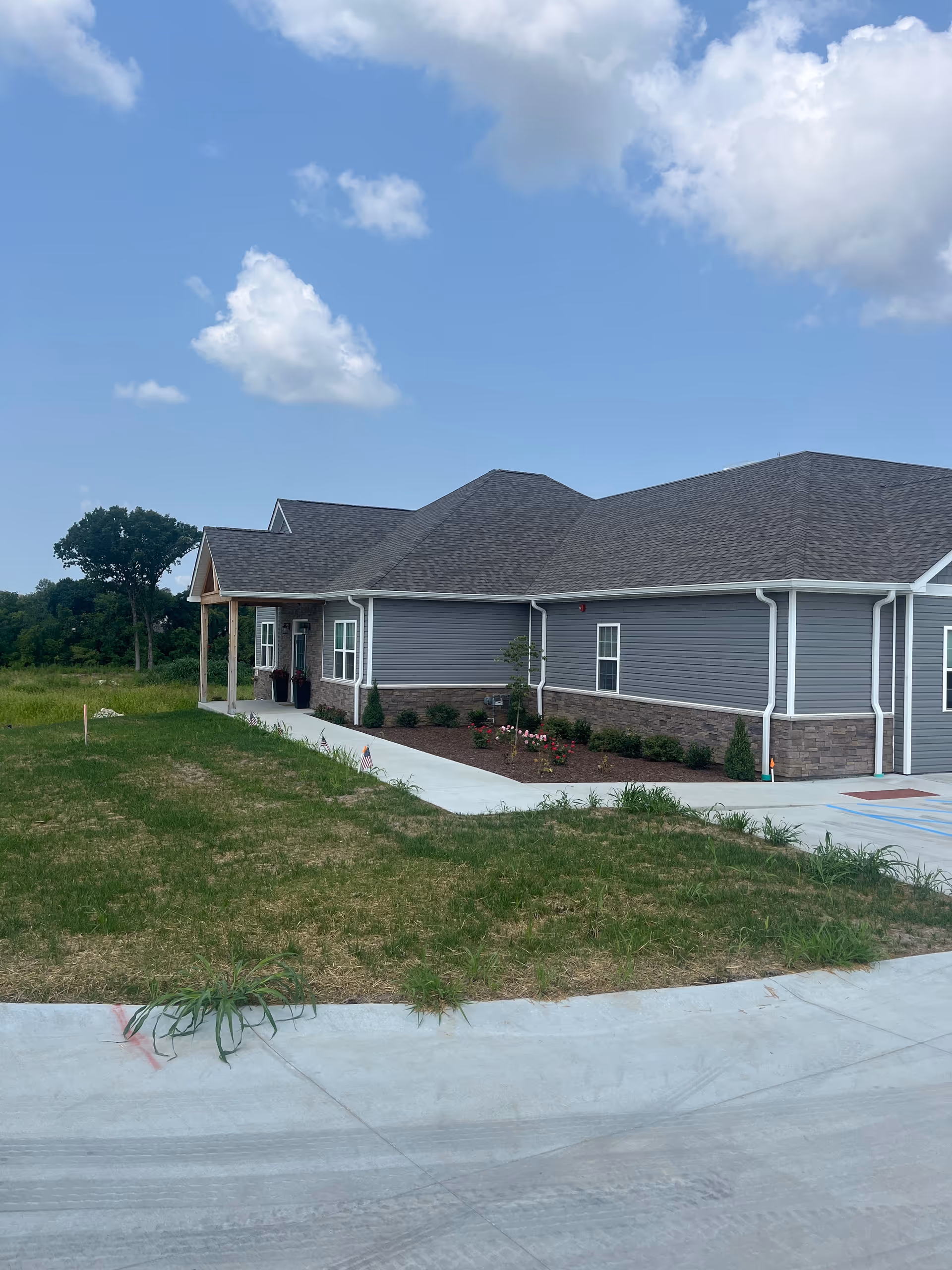 A single-story gray senior housing building with landscaping and a clear blue sky.