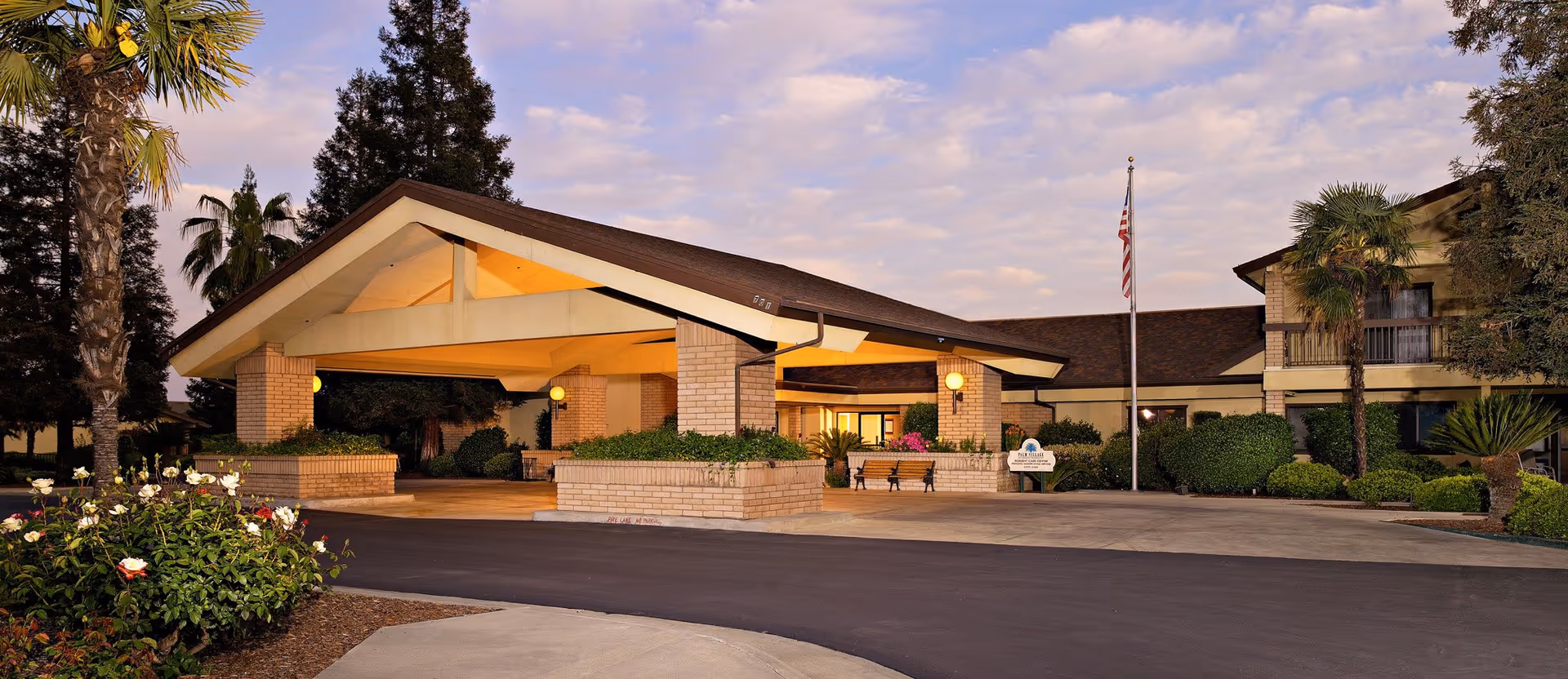 Exterior view of Palm Village Retirement Community entrance with a covered porte-cochere and landscaping.