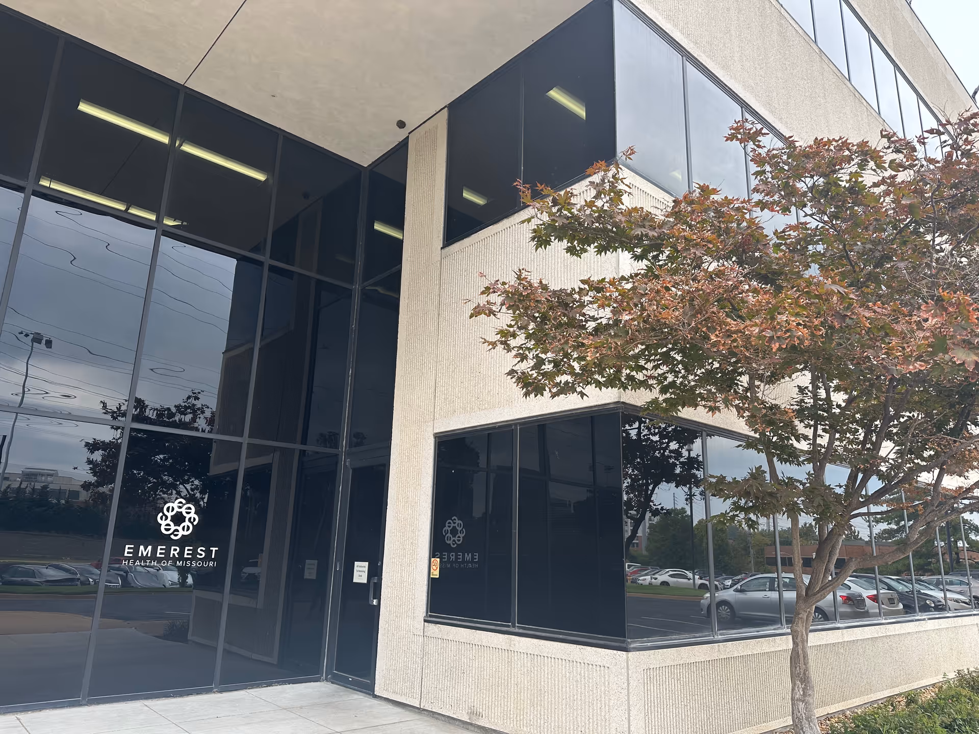 Modern glass-front building with Emerest Health of Missouri logo and surrounding trees.
