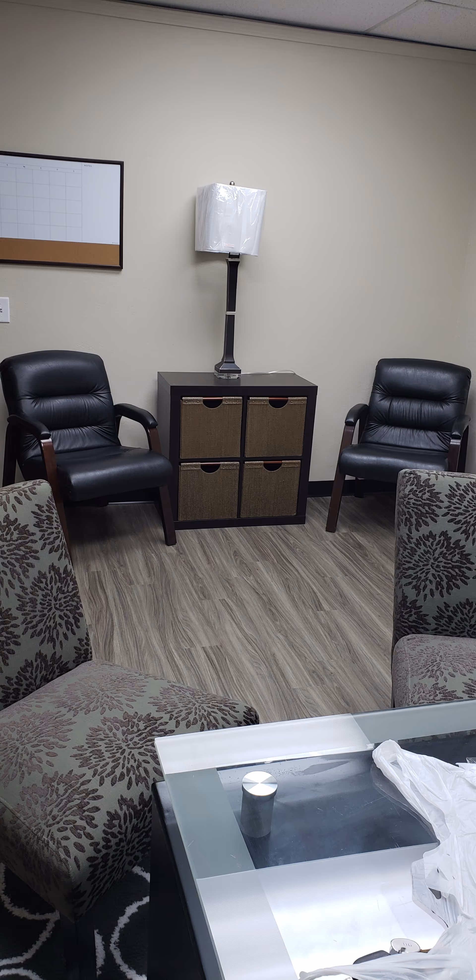 A small waiting area with two black leather chairs, a cabinet, and a lamp.