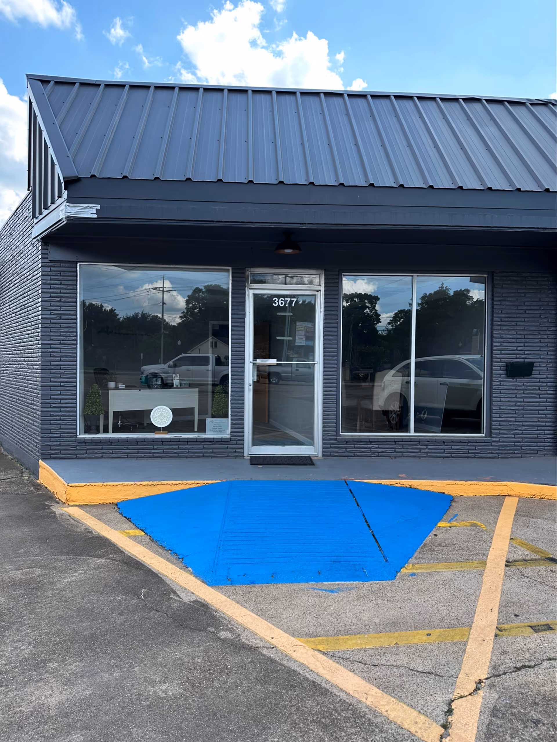 Gray brick building storefront with glass door, large windows, and a blue ramp outside.