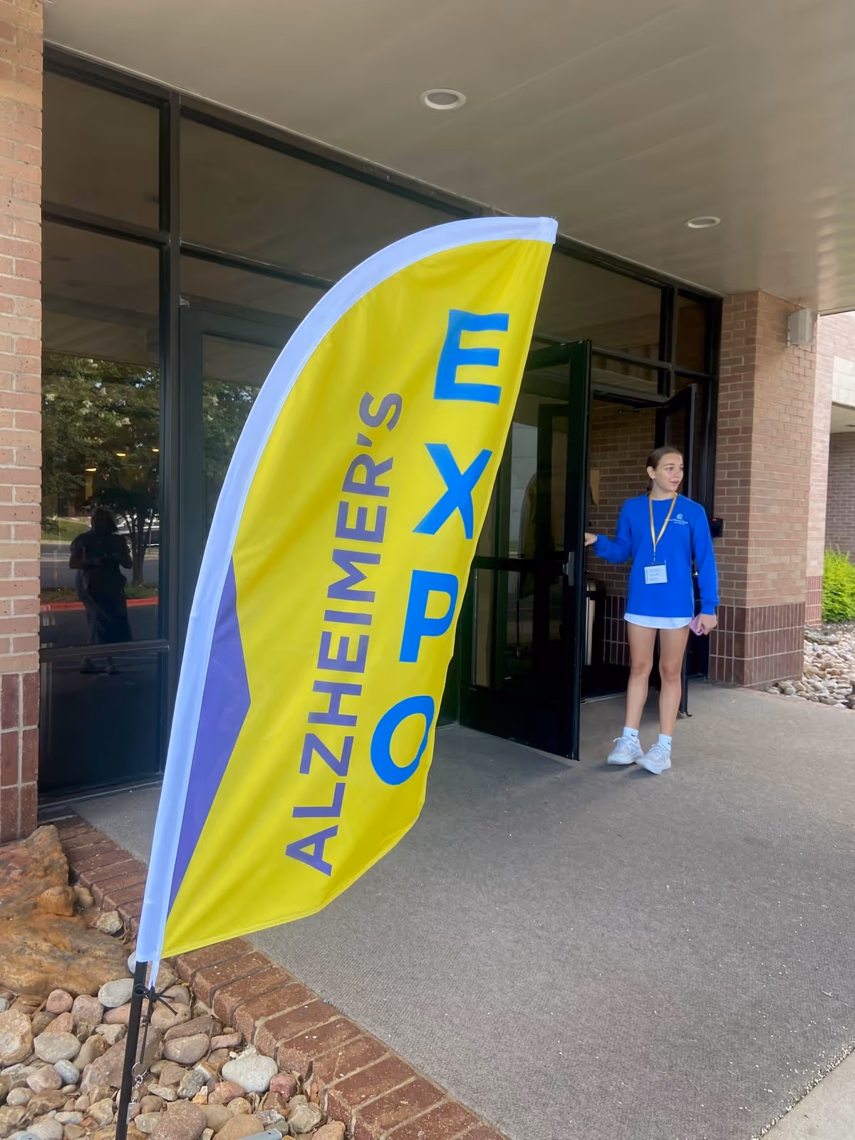 Bright yellow Alzheimer’s expo banner outside facility entrance with a staff member nearby.