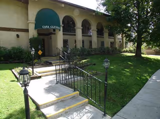Front entrance of a senior living facility with arched windows, green awning, and steps.