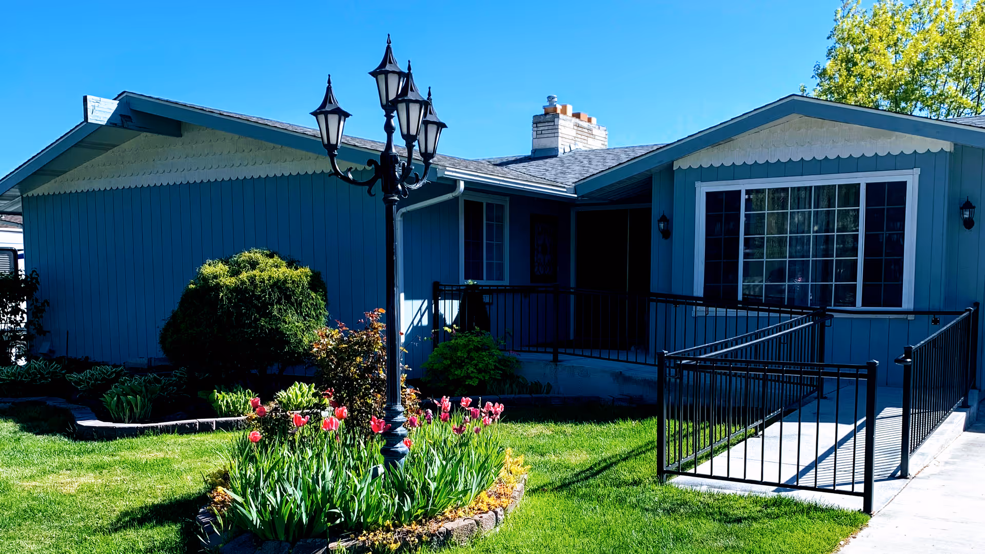 Blue single-story facility front with a ramp, garden, and decorative lamppost.
