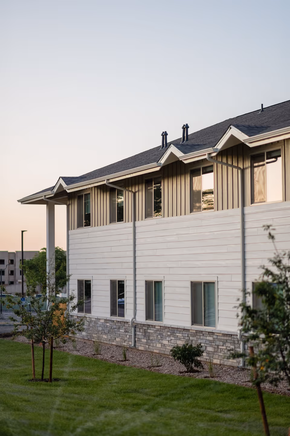 Two-story modern senior living facility exterior with white siding, stone base, and landscaping.