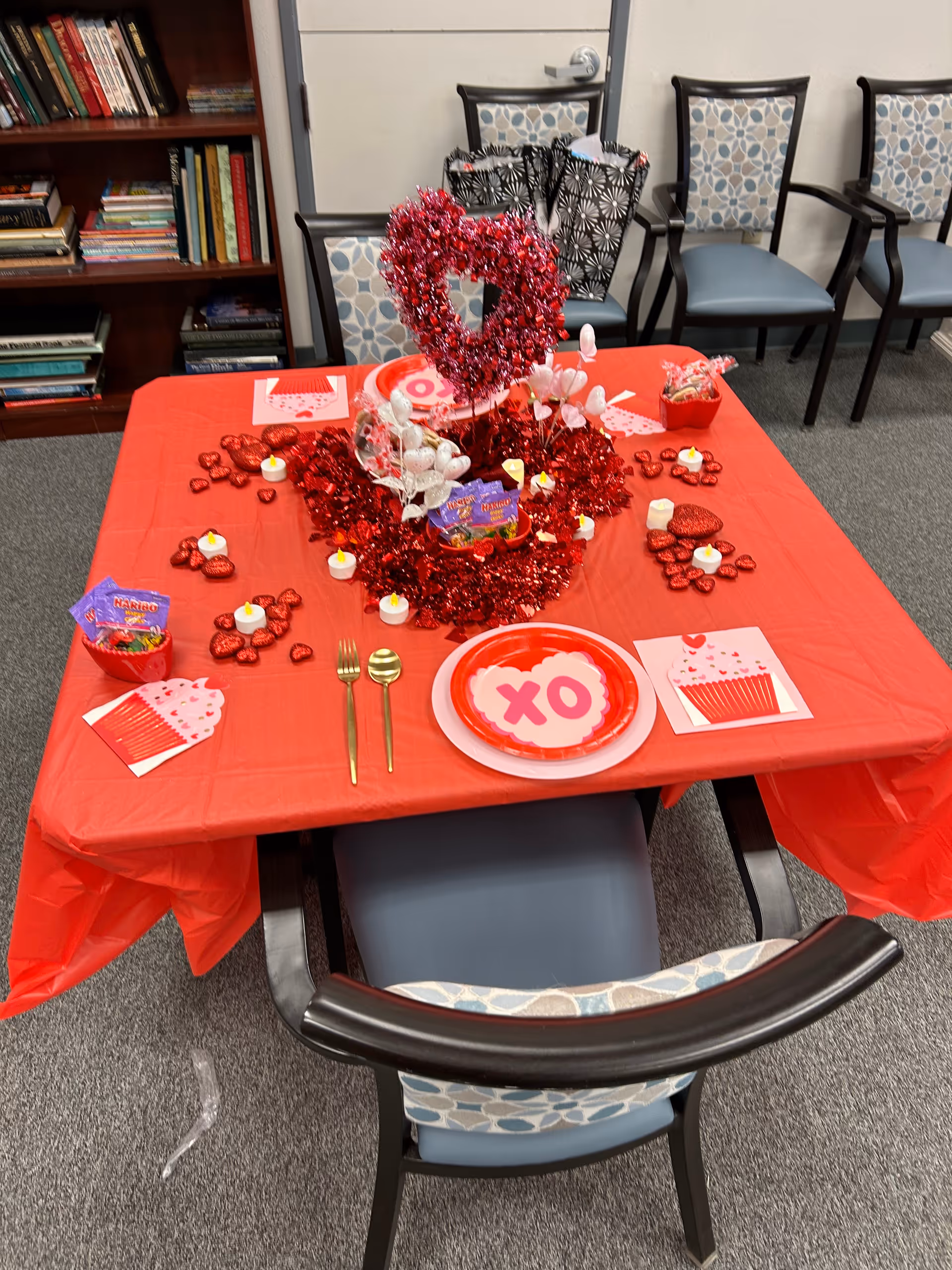 Valentine's Day-themed dining table with red decorations, heart centerpiece, plates, and chairs in an interior room.