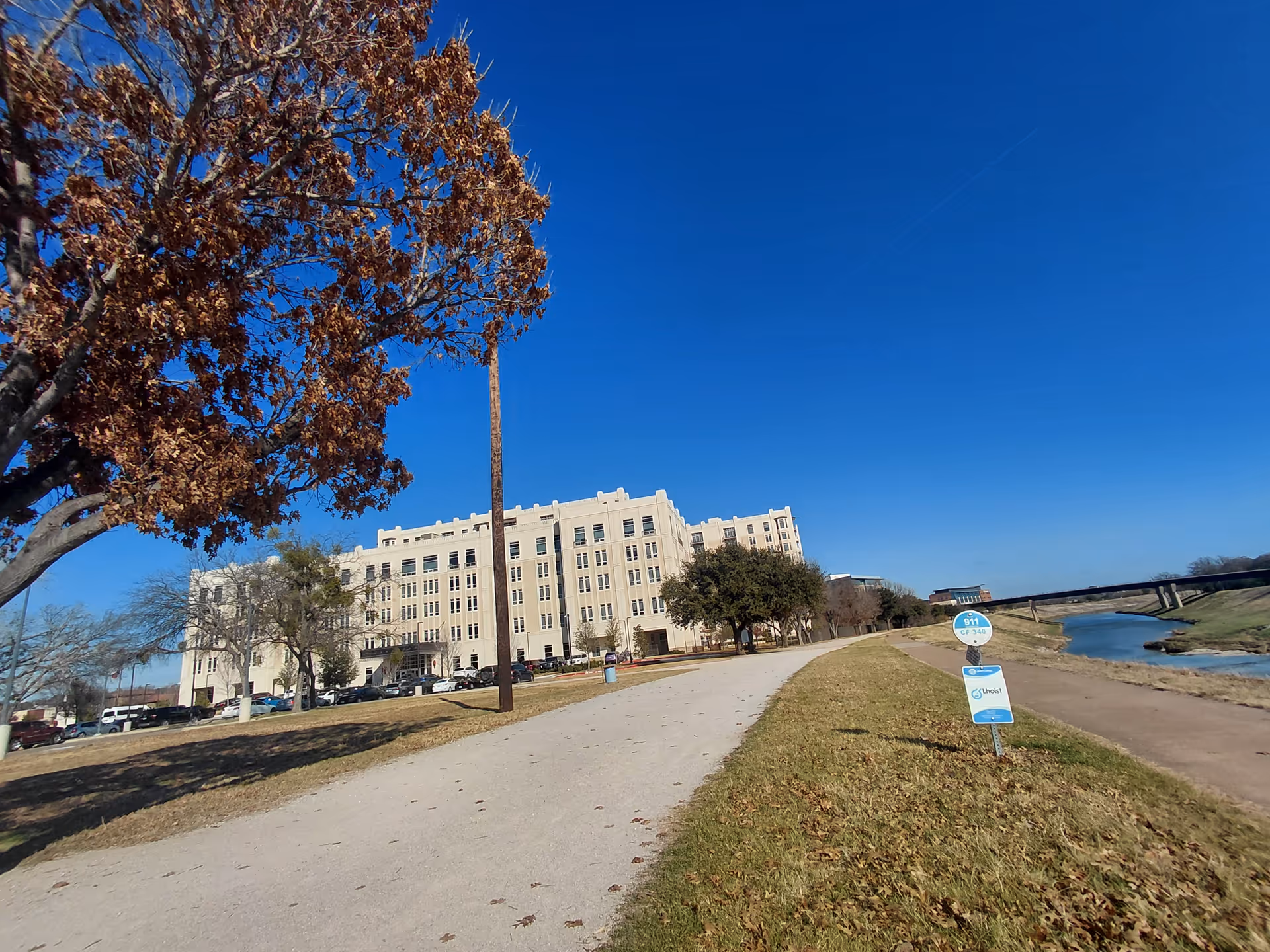 Exterior view of a large beige senior living facility beside a river path.