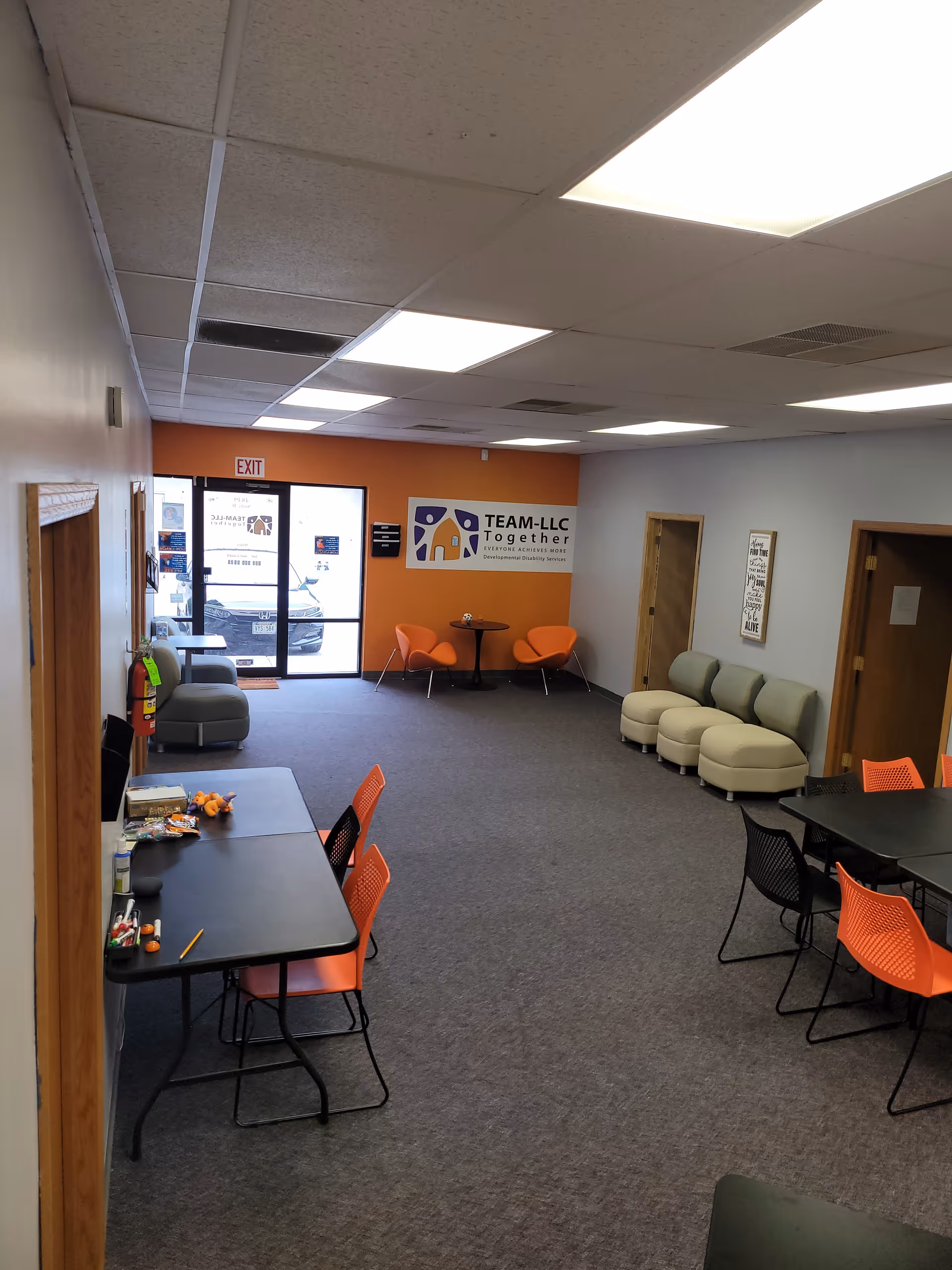 Indoor lounge area with orange chairs, tables, and a Team-LLC Together sign.