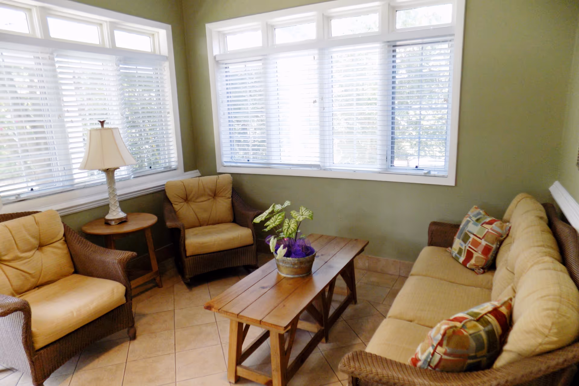 Cozy living room lounge with wicker chairs, beige sofa, and a coffee table by large windows.
