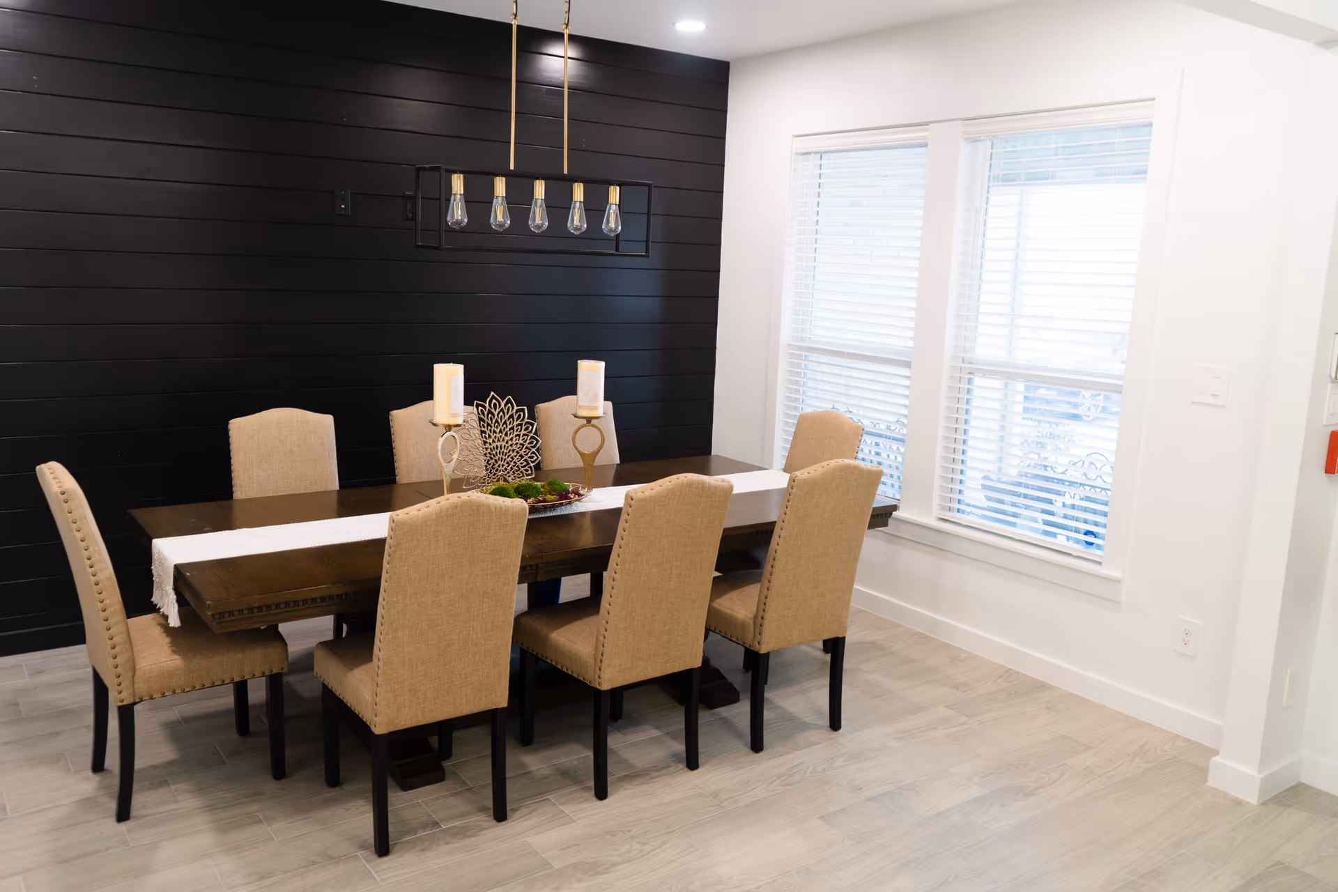 A modern dining room with a long table, beige chairs, and a dark accent wall.