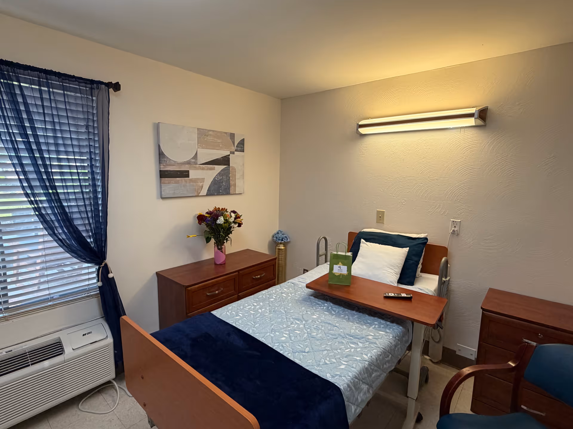 Single patient bedroom in a nursing center with bed, dresser, and blue curtains.