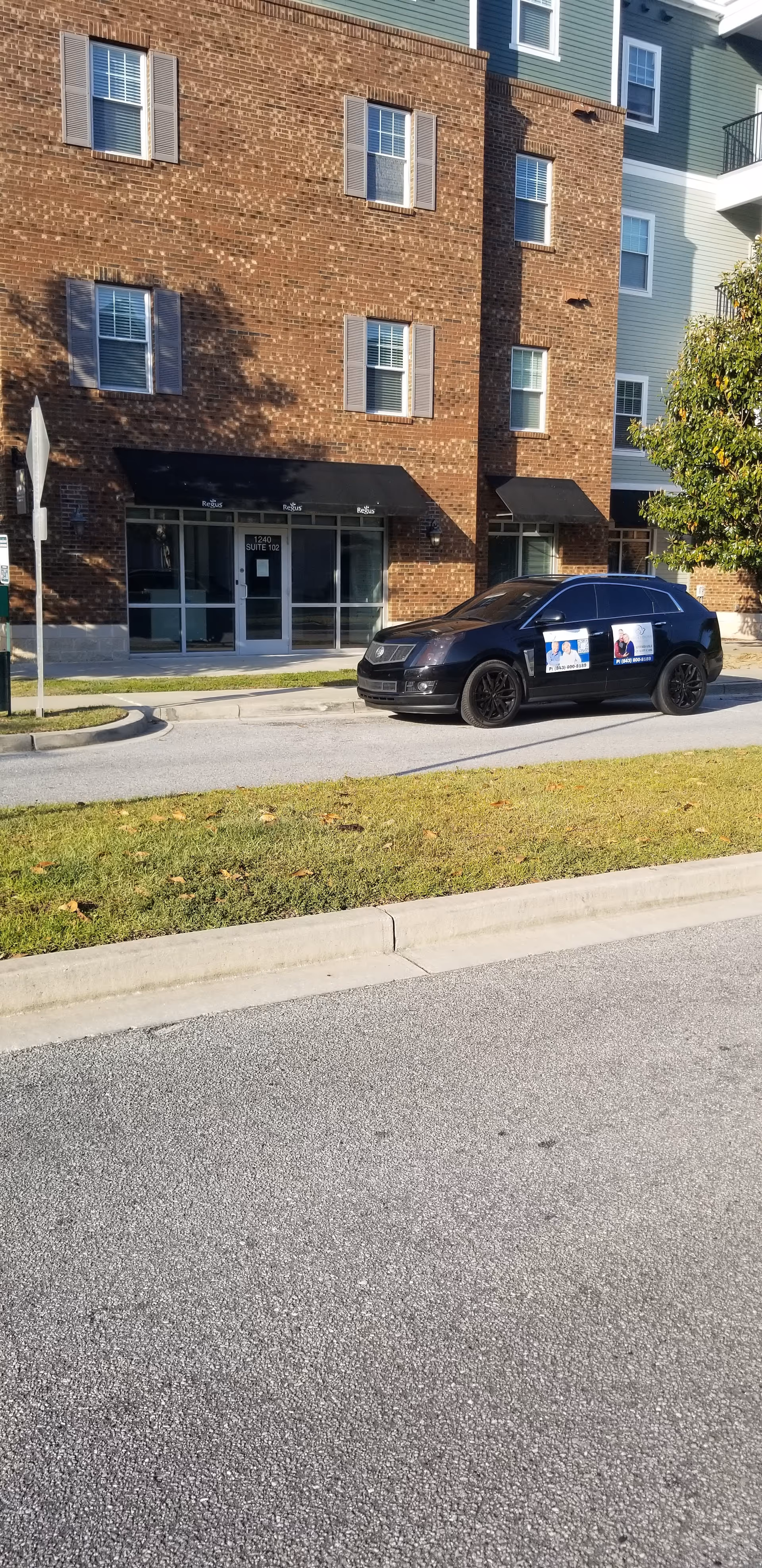 Brick senior living building with a dark car parked along the sidewalk.