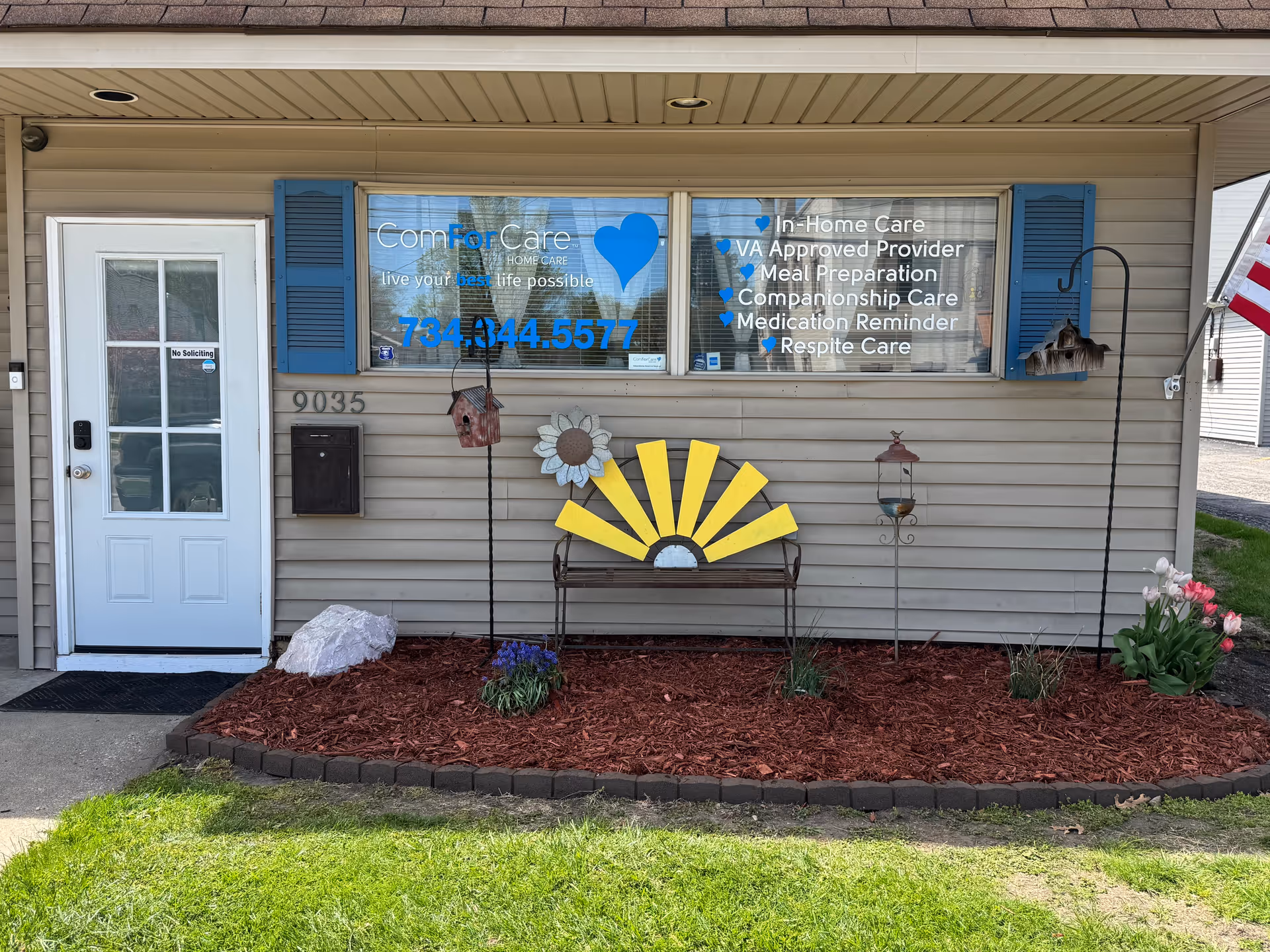 Front of ComForCare Home Care Monroe with window sign, bench, and flower bed.