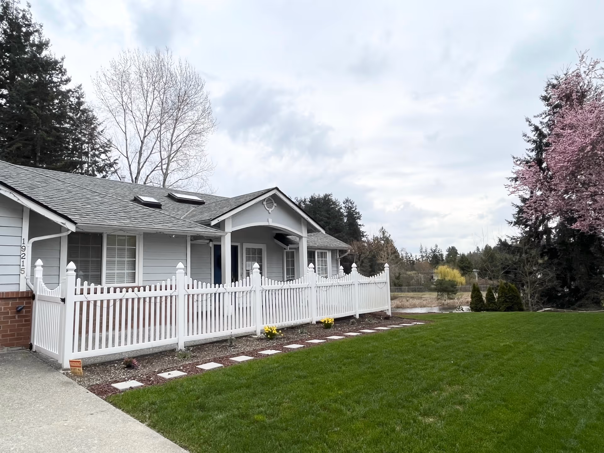 Single-story facility with a white picket fence, green lawn, and trees in front.