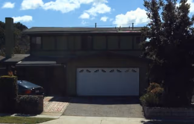 Two-story suburban home with a white garage door, driveway, and surrounding shrubs.