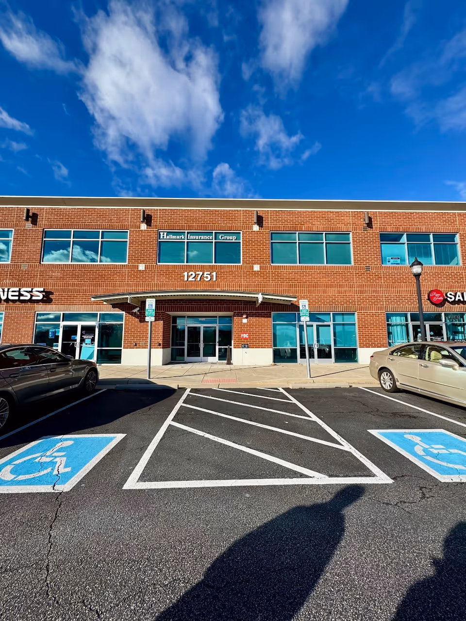 Brick commercial building with large glass windows and a glass entrance, handicapped parking in the front.