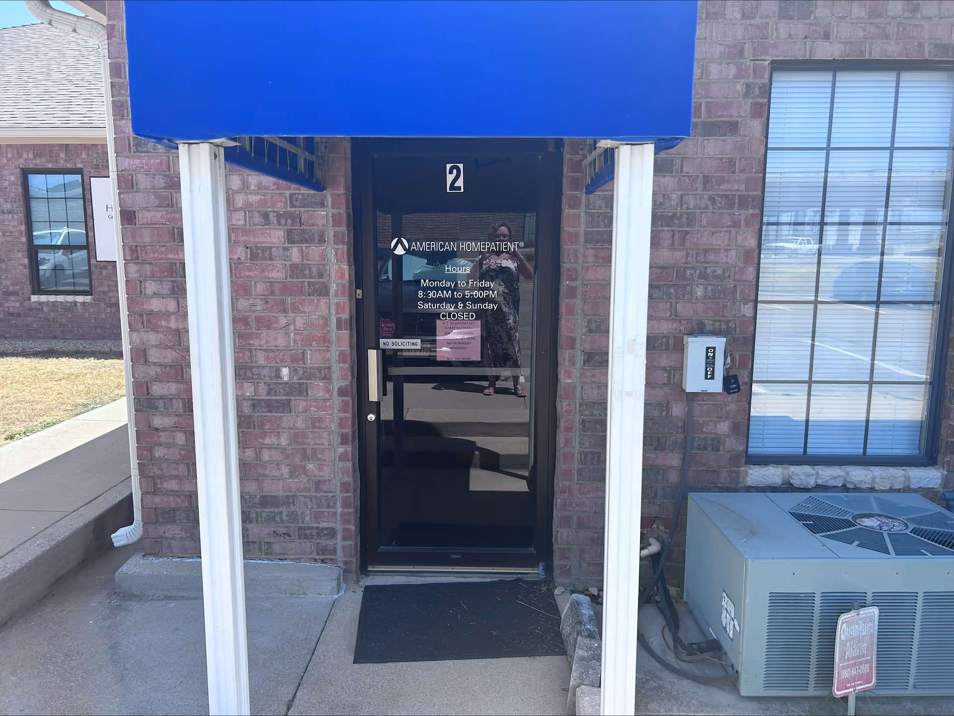 Brick front entrance with blue awning and glass door labeled American Home Patient.