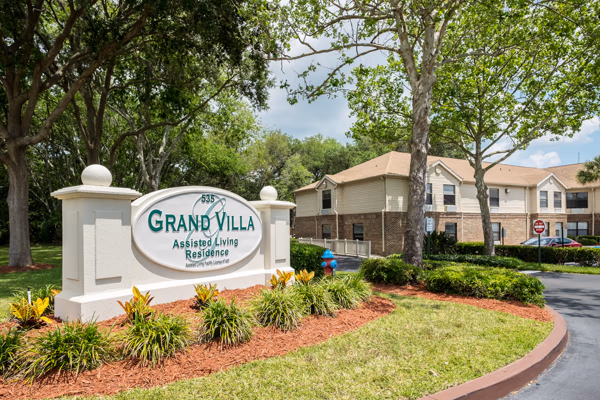 Grand Villa of Ormond Beach entrance sign with landscaped curb and building in background.